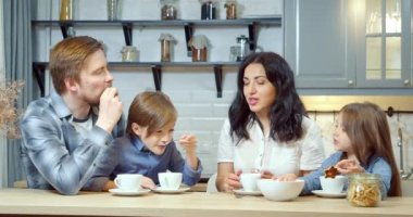 Mutlu aile anne ve baba ve iki sevimli çocuk birlikte evde mutfakta vakit geçirirken ev yapımı kurabiyelerle çay içiyorlar..