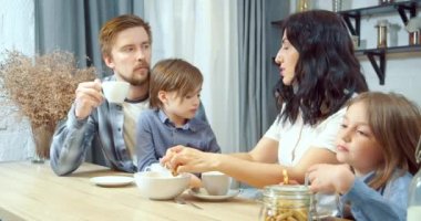 Mutlu aile anne ve baba ve iki sevimli çocuk birlikte evde mutfakta vakit geçirirken ev yapımı kurabiyelerle çay içiyorlar..
