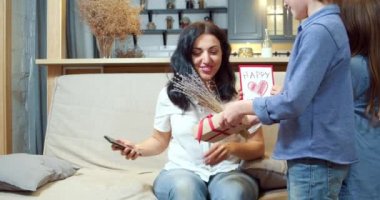 İki tatlı çocuk annelerini Anneler Günü 'yle kutluyor ve el yapımı kartla kalplerini kapatıyorlar. Mutlu bir aile evdeki kanepede sarılıp öpüşüyor..