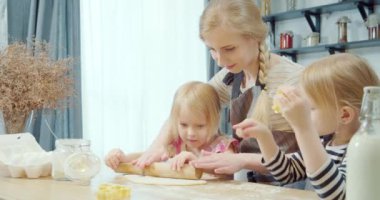 Mutlu bir aile, genç bir anne ve iki küçük kız ev yapımı kurabiyeler pişiriyorlar. Evdeki mutfakta birlikte hamuru yuvarlıyorlar..