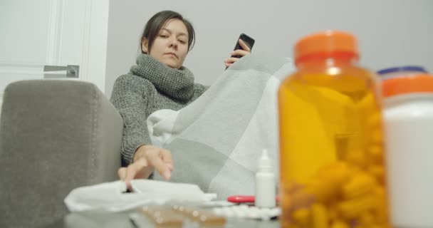 自宅のソファに座っている間 若い病気の女性が鼻水や咳をして通信のためのスマートフォンを使用して — ストック動画