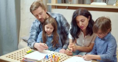 Mutlu yaratıcı aile, renkli kalemler ve keçeli kalemlerle çizim yapan iki sevimli çocuk. Evdeki kanepede birlikte oturuyorlar..