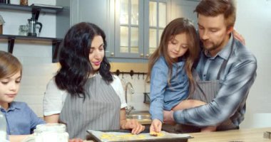 Mutlu aile pişirme tepsisine koyarak ev yapımı kurabiyeler hazırlıyor. Mutfakta ebeveynlere yardım eden iki tatlı çocuk..