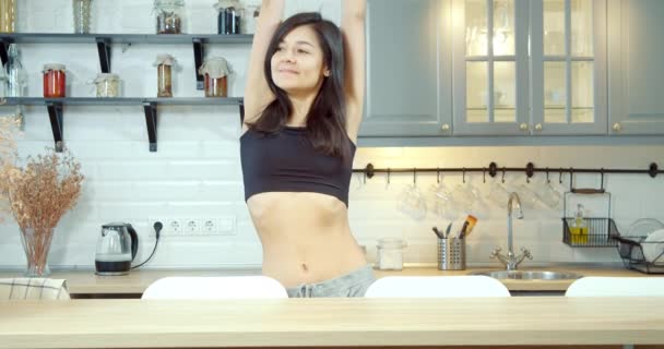快乐迷人的女人一边伸懒腰一边喝水 一边在厨房里享受着早晨的快乐 — 图库视频影像