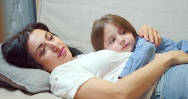Önemseyen bir anne evdeki kanepede uzanmış küçük kızını kucaklıyor ve okşuyor. Annelik kavramı.