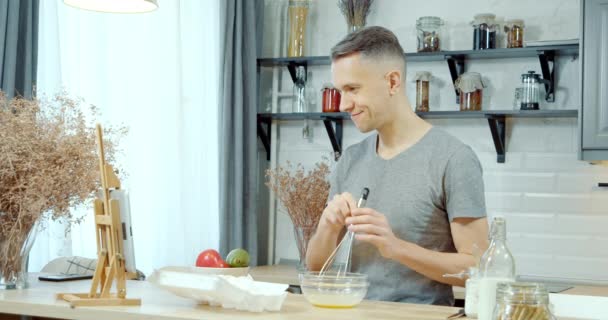 Młody Przystojny Mężczyzna Przygotowuje Ciasto Naleśniki Lub Ciasteczka Pomocą Tabletu — Wideo stockowe