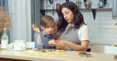 Genç bir anne oğluyla ev yapımı kurabiyeler hazırlıyor hamuru yoğuruyor ve mutfaktaki kurabiye kesicilerle figürleri kesiyor..