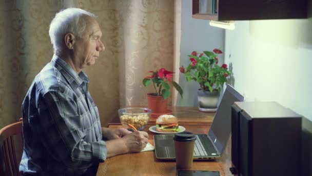 Anciano Trabajando Portátil Tomando Notas Cuaderno Mientras Está Sentado Una — Vídeo de stock