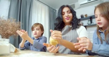 Mutlu aile kurabiye için hamur hazırlıyor. İki tatlı kız ve erkek çocuk mutfakta anneme yardım ediyor..