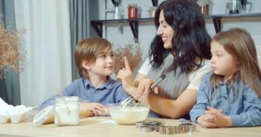 Mutlu aile anne ve iki çocuk mutfakta birlikte ev yapımı kurabiyeler pişirirken eğleniyorlar.
