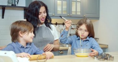 Mutlu aile annesi ve iki çocuk mutfakta birlikte ev yapımı kurabiyeler hazırlıyorlar. Annesi ve kardeşinin gözetiminde çırpılmış yumurta çırpan tatlı küçük kız..