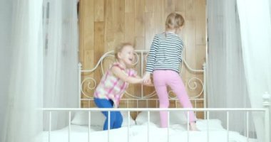 İki komik küçük kız evde birlikte eğlenirken yatakta gülüp zıplıyorlar..