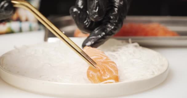 皿の上の新鮮なサーモンフィレのクローズアップ 料理人の男性の手は台所でサーモンの破片を敷設 — ストック動画