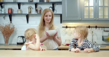 Genç anne mutfakta iki tatlı kızına taze pişmiş kurabiye ikram ediyor..