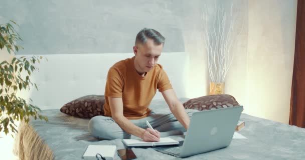 Unge Man Som Jobbar Bärbar Dator Och Antecknar Anteckningsbok Hemma — Stockvideo