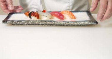 Taze suşi, balık ve deniz ürünleri tabakta. Erkek aşçı, eldiven giymiş Japon yemekleri servis ediyor.