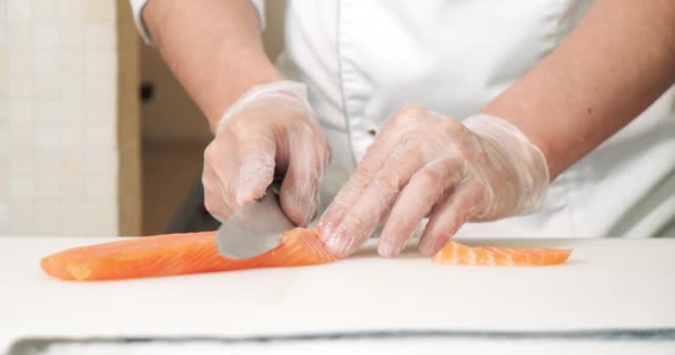 Közelkép férfi szakács kéz kesztyű vágás lazac filé késsel fehér táblán.