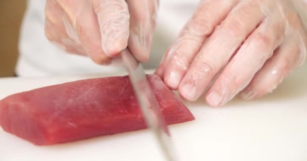 近くの男性料理人の手で手袋を切ってマグロの切り身とナイフで白いボード — ストック動画