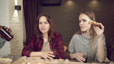 Bir grup çok ırklı arkadaş pizza yiyor, bira içiyor ve evdeki oturma odasında sohbet ediyorlar..
