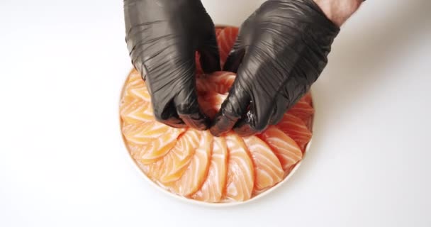 皿の上にダイコンのサラダに新鮮なサーモンのスライスを敷く手袋で調理の手のクローズアップ — ストック動画