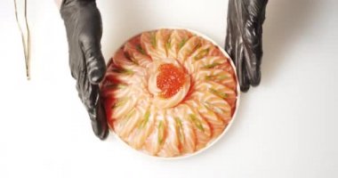 Eldivenli aşçının elleri bir tabak daikon salatası ve yeşil ve kırmızı havyarlı somon dilimleri servis ederken..