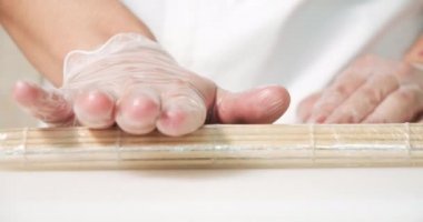 Masaya suşi ruloları yapmak için eldiven takmış, bambu hasırı seren erkeklerin ellerini kapatın..