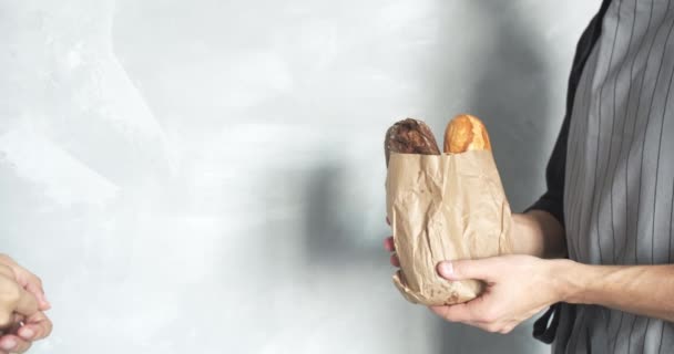 面包师或卖家的男性手拉着包 给女人一个灰色背景的美味的面包包 复制空间 — 图库视频影像