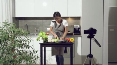 Çekici genç kadın evdeki mutfakta dijital kamerada sağlıklı beslenmeyle ilgili bir video kaydediyor. Vlog ve sosyal medya kavramı