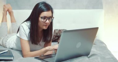 Laptop klavyesinde yazan genç bir kadın. Serbest çalışan kadın ya da öğrenci evdeki yatakta yatan sosyal ağlarda yorumlar yazıyor..