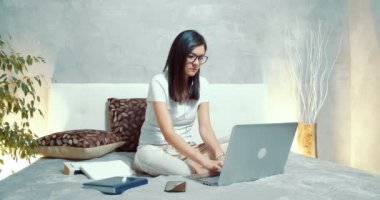 Laptop klavyesinde yazan genç bir kadın. Sosyal ağlarda yazı yazan serbest çalışan kadın ya da öğrenci evdeki yatakta oturuyor..