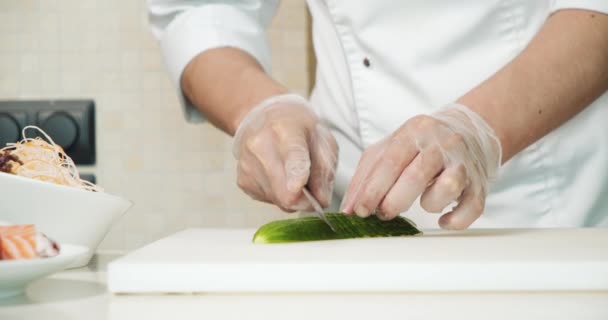 一个戴着手套的厨师用一把刀在白板上切黄瓜 把他的男性手包扎起来 — 图库视频影像