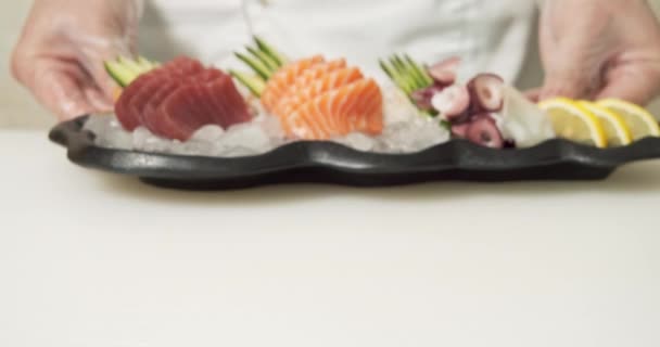 新鮮な魚とタコのスライスの皿を氷の上に野菜と手袋で男性シェフの手のクローズアップ — ストック動画
