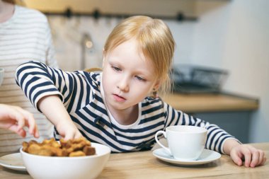 Küçük tatlı kız mutfakta kahvaltı ederken ev yapımı taze kurabiyeler yiyor..