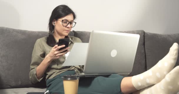 여자가 집에서 노트북으로 일하면서 스마트폰 보고서를 작성하거나 종이에 계획을 세우고 — 비디오