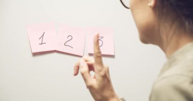 Gri bir duvara 12-3 numara yapıştırılmış pembe çıkartmalar. 2 numarayı seçen kadın..