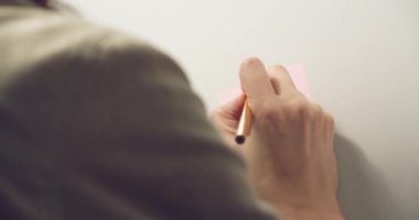 Pembe bir çıkartma yapıştıran ve üzerine bir hatırlatma notu yazan kadın elleri..