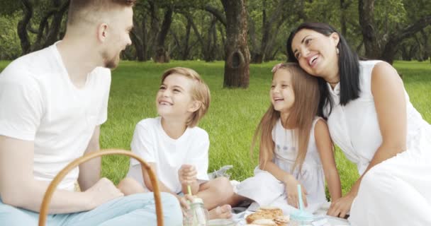 絵のように美しい緑の庭でピクニック中に芝生の上で休んでいる子供たちと幸せな家族 — ストック動画