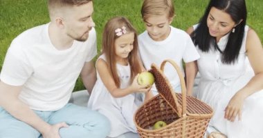 Mutlu bir aile ve çocuklar yeşil bahçedeki piknik sırasında çimlerin üzerinde dinleniyorlar. Açık havada.