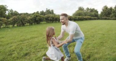 Mutlu baba kusuyor ve parkta küçük şirin bir kız çeviriyor. Baba ve kızı çimenlerde oynuyorlar. Mutlu aile birlikte.