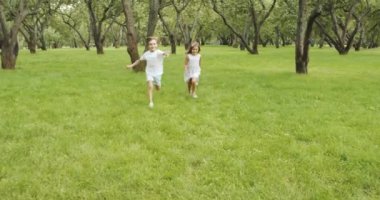 İki mutlu çocuk çimenlerde koşuyor kameraya bakıyor ve bahçede el sallıyor. Tatil, yaz ve macera konsepti.