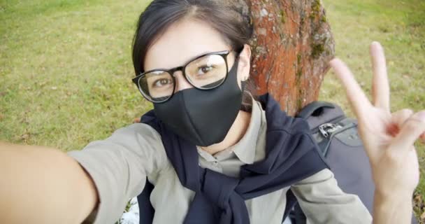 公園を歩いている間に自撮りを作る保護マスクの若い女性 友人とのビデオチャット会議 Covid後の観光客 Covid 隔離中の生活 — ストック動画