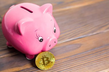 Bir altın bitcoin sikke koyu kahverengi ahşap arka plan yeni sanal para ile pembe piggy banka