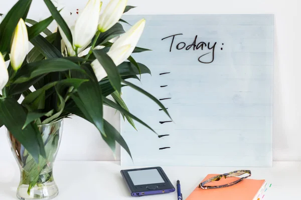 Turuncu defter, glassses, mavi e-kitap için bugün planları resepsiyon ile ve güzel Beyaz lilyum beyaz masada, bugün kavramı listelemek için bir buket.