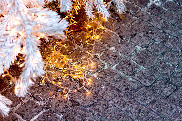 Silver Christmas tree with golden shining garlands against the background of pavers