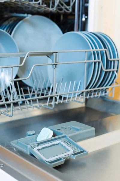 Відкрита посудомийна машина з посудом та екологічно-зеленою посудомийною машиною. Вертикально. Екологічний миючий засіб для посудомийної машини . — стокове фото