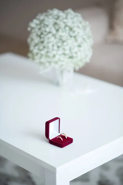 Wedding rings in a red velvet box and bridal bouquet over a white table - selective focus, copy space, vertical orientation