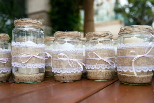 Wedding decoration - candles in glass jars decorated with lace, sackcloth and ribbons over wooden table