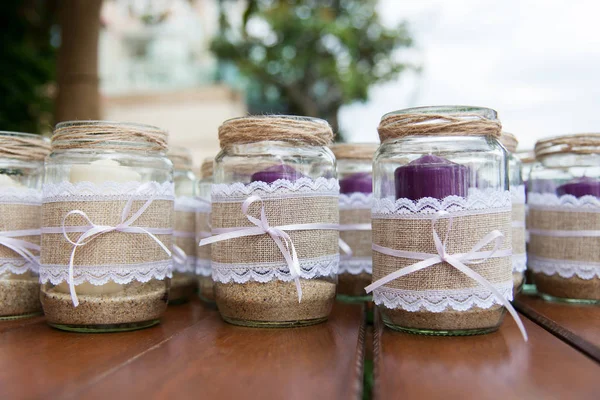 Wedding decoration - candles in glass jars decorated with lace, sackcloth and ribbons over wooden table