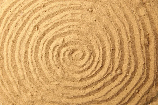 Spiral drawing on beach sand background. Spiral pattern on golden sand. Sand texture.