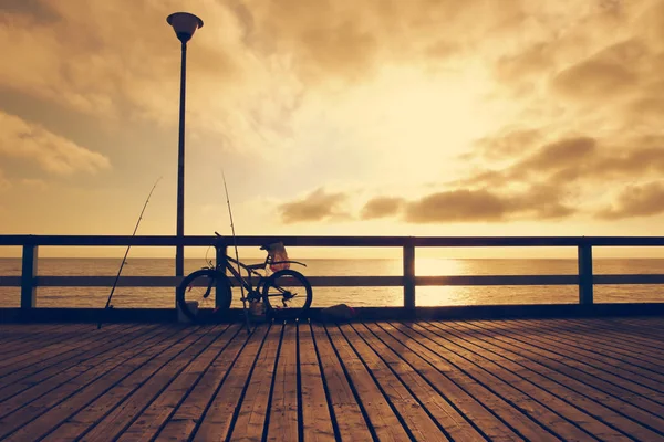 Fisherman bicycle with fishing rods on wooden bridge. Toned. Bicycle on sea bridge at sunset.